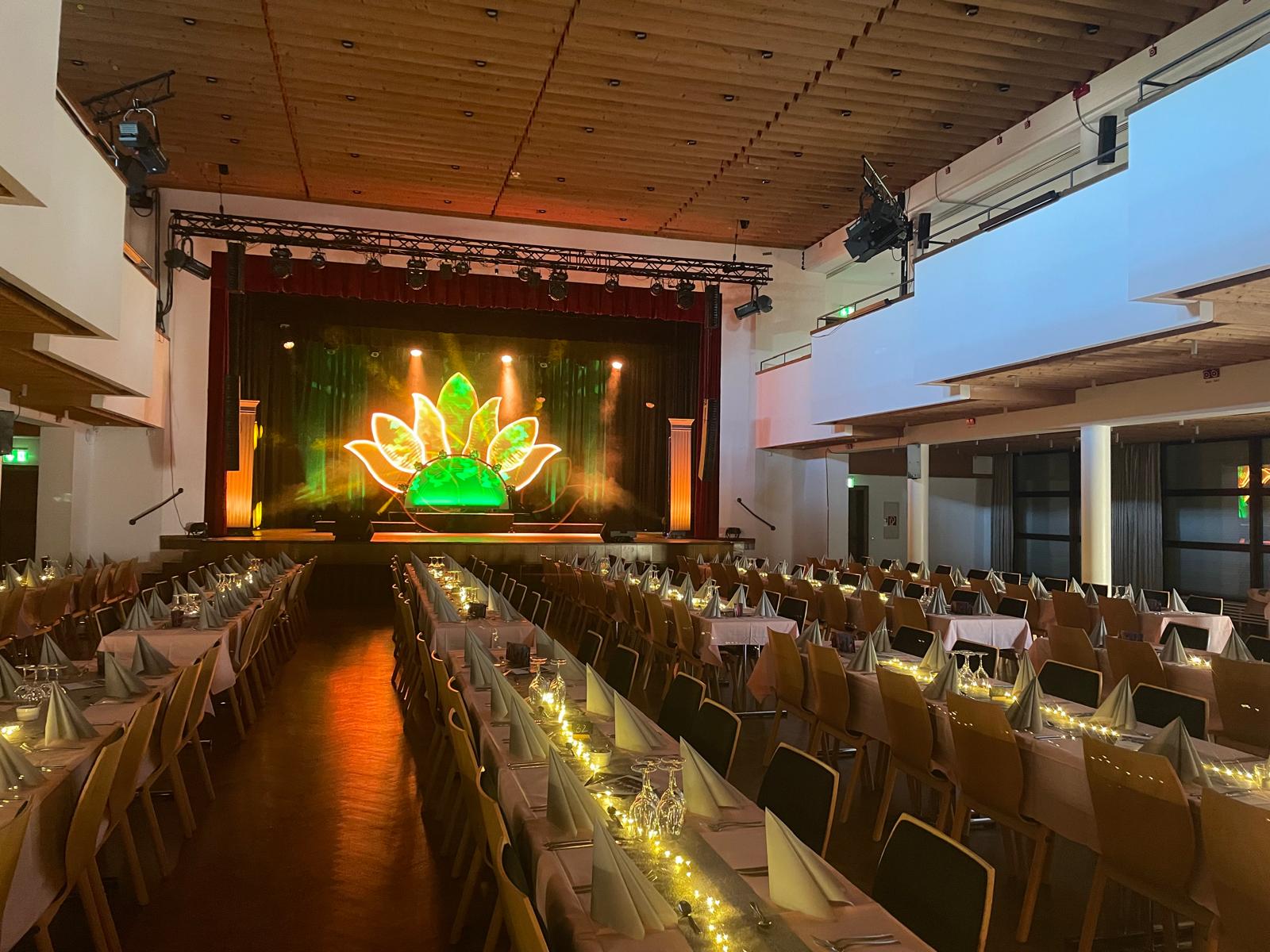 Eingedeckter Saal mit grün-gold leuchtendem Bühnenbild